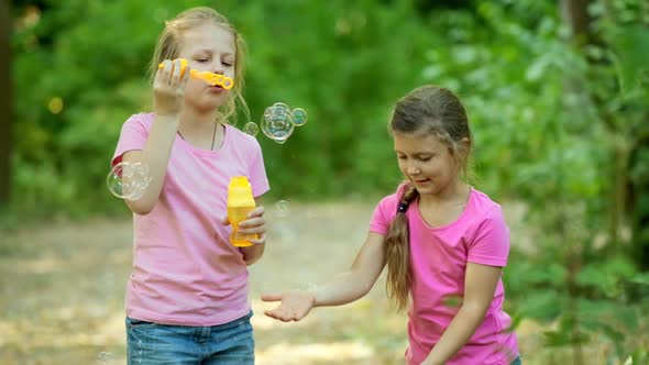 Two little girls blowing bubbles and playing in the Park. Happy childhood concept. Slow motion