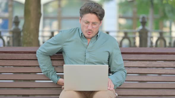 Man having Back Pain while using Laptop, Outdoor alt