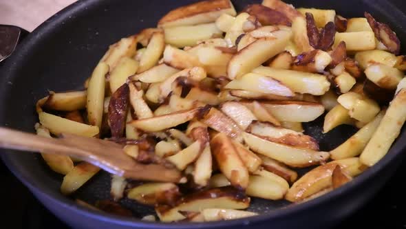 Frying and Stirring Homemade French Fries in Pan on Kitchen Stove