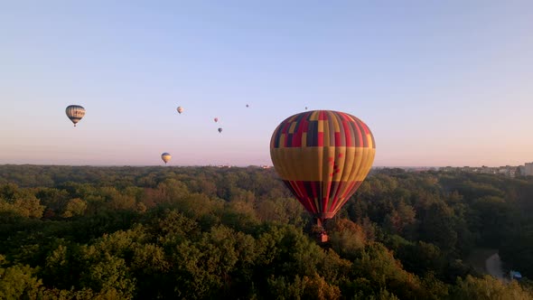 Colorful Hot Air Balloons Flying Over Green Park in Small European City at Summer Sunrise, Aerial alt