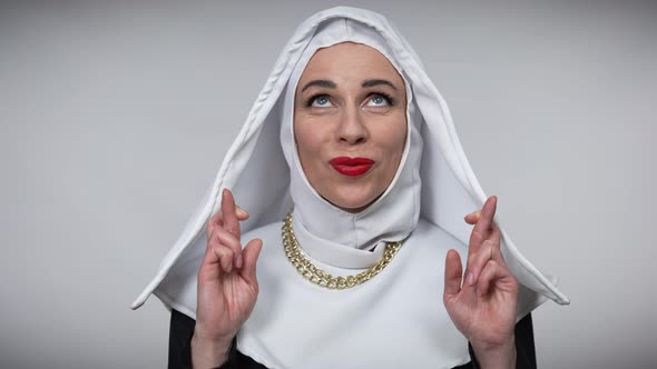 Smiling Woman in Nun Costume Crossing Fingers in Hope Gesture Looking Up Wishing Praying alt