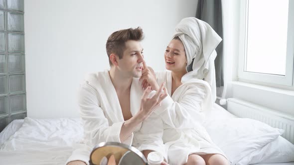 Morning Preparing of Beautiful Caucasian Couple in Bathrobe Use Moisturizing Cream
