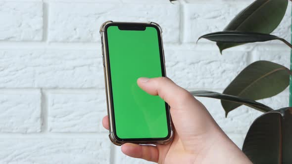 Man Using Smart Phone in Office Space Sitting on Chair and Using Green Screen Phone Mockup Chroma alt