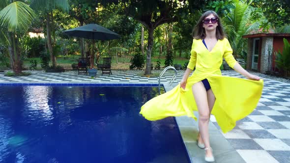 Asian Woman in Yellow Walks Along the Pool alt