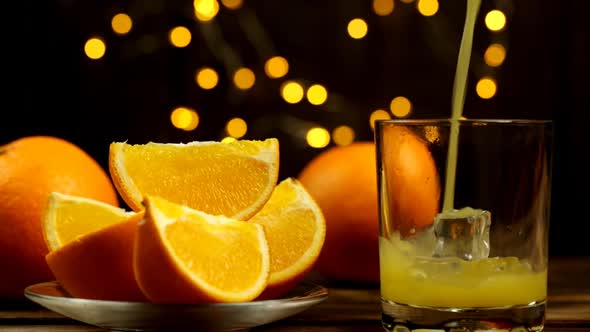 Pieces Of Orange And Juice Are Poured Into A Glass With Lights In The Background