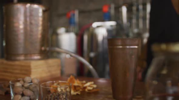 Caucasian man working at gin distillery, wearing apron, connecting pipe to distillation equipment alt