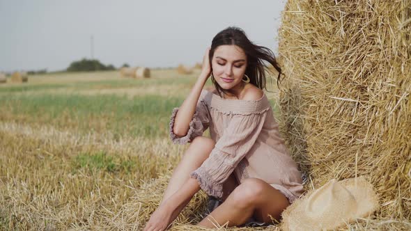 Lady in Dress Resting at a Haystack in a Field and Correcting Hair with Laugh alt