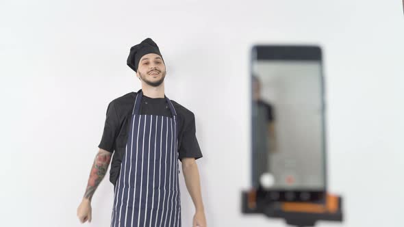 Smiling Professional Male Chef in Apron and Hat Ending Online Lesson Streamed on Smartphone alt