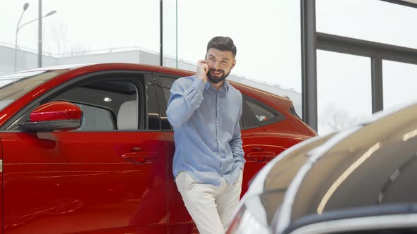 Charming Man Talking on His Smart Phone While Choosing New Car at the Dealership