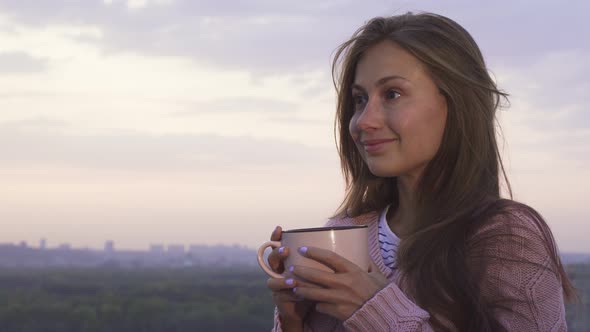 A Young Girl Drinks a Warm Drink and Enjoys the Sunset alt