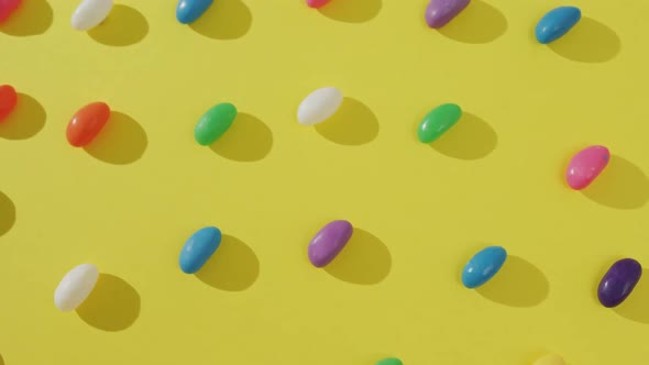 Video of overhead view of rows of multi coloured sweets over yellow background alt