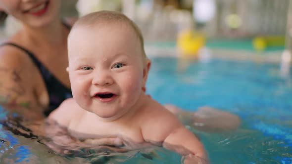 Happy Mother in Red Swimming Suit with Baby Son Surfing Water with Fun in Swimming Pool alt