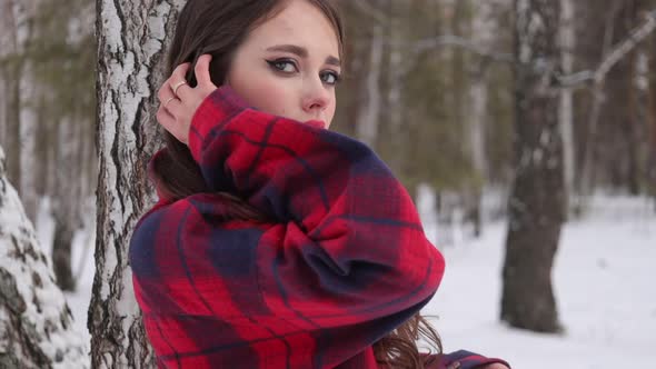 Young Woman with Wavy Hair Standing and Touching Face in Winter Forest