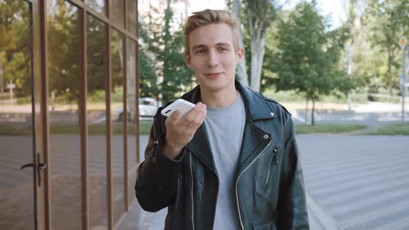 Recording voice message. Talking on the mobile phone. Walking up the street in the city. alt