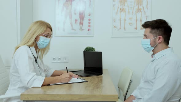 In Doctor Office Man Patient in Medical Mask Talks to His Female Doctor alt