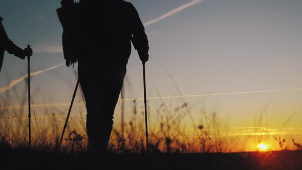 Silhouettes of Two Hikers with Backpacks Enjoying Sunset View From Top of a Mountain. Enjoying the alt