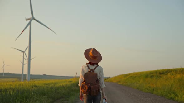 Young photographer with a camera walking near a field with alternative green energy windmills alt