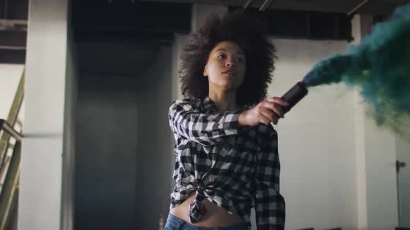 Mixed race woman holding green flare standing in an empty building alt