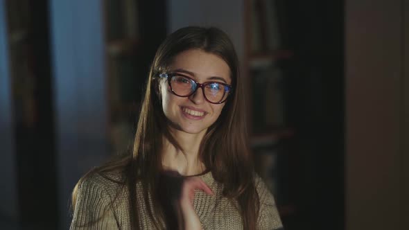 Girl with Glasses Tucks Her Hair Behind Her Ear and Laughs at Camera in Library alt