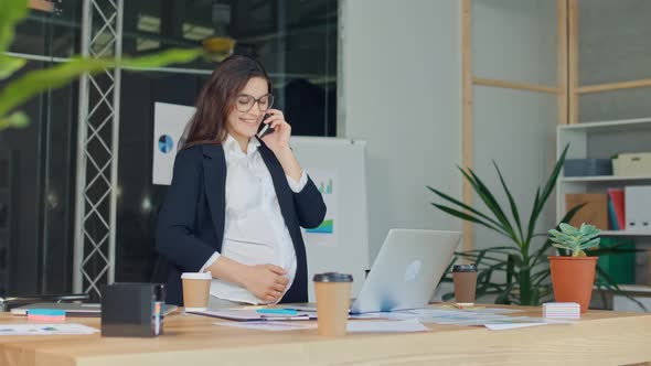A Beautiful Pregnant Woman Talking on a Cell Phone Sitting at a Table alt