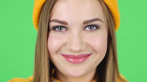 Woman in a Yellow Hat Is Looking Straight, Smiling and Blinks. Close Up. Green Screen alt