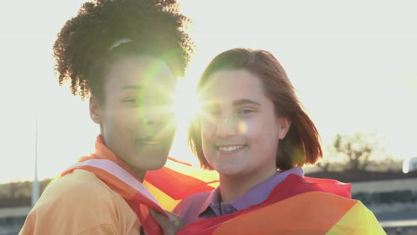 Mulitracial lesbian girls kissing together at gay pride parade while holding rainbow flag