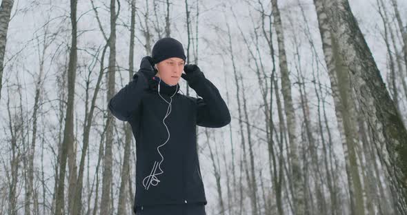 A Young Man on a Morning Jog Holds Headphones in His Hands and Inserts It Into His Ears Before alt