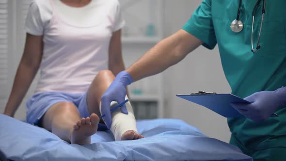 Doctor Checking Injured Patients Leg in Elastic Wrap, Writing Examination Result