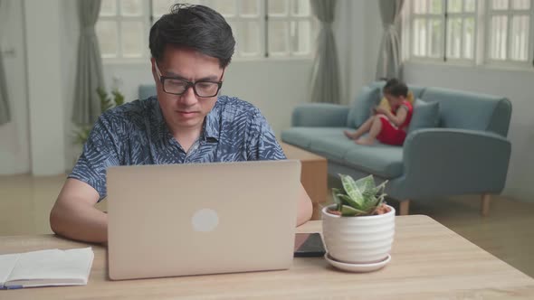 Asian Man Working With Laptop Computer And Son Use Mobile Phone alt