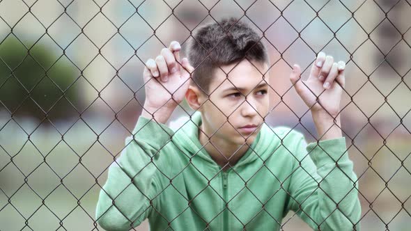 Refugee Sad Boy Stands Alone Head Bowed Near the Fence Dropped Eyes Cinematic Shot