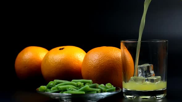 Pour Orange Juice Into A Glass With Ice And Three Oranges Nearby And Beans