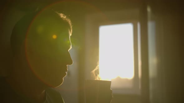 Silhouette of a man with a mug of hot coffee, sun glare, camera movement alt