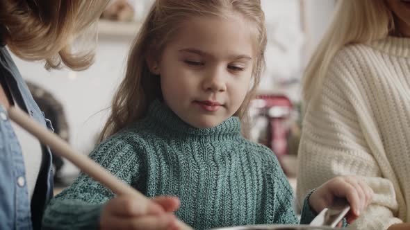Close up video of little girl cooking with mother and grandmother. alt