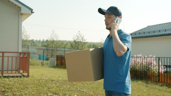 Slow Motion of Delivery Guy Speaking on Mobile Phone Carrying Parcel in Suburban Area alt