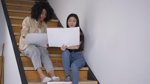Young Confident Women Discussing Business Startup Idea Sitting on Stairs in Home Office alt