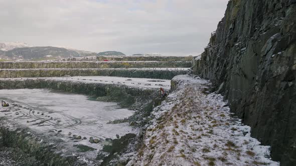 Excavator digging inside a snowy quarry. Heavy machinery on pit. Tracked vehicle alt