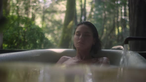 A girl in a bathtub in a forest during the rain. Beautiful young woman relaxing in the bathroom