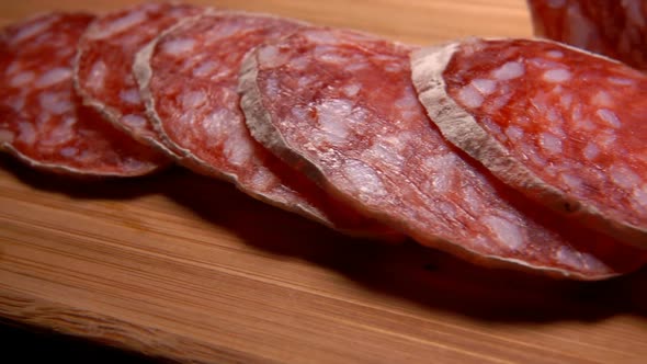 Fork Takes Slice of Dried Sausage From wooden Board alt