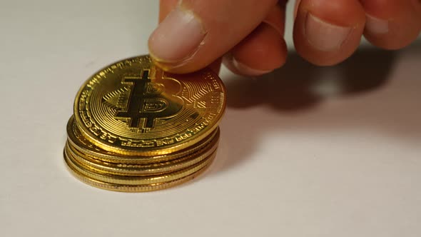 A man's hand stacks gold Bitcoin cryptocurrency coins in a column on a white background alt