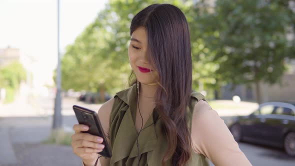 Young Asian Woman Listens To Music Earphones Smartphone Urban Area alt