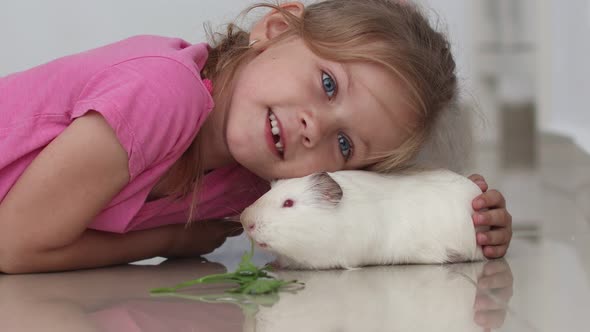 Side View Child Little Girl Plays Strokes Guinea Pig Pet Lying on the Floor