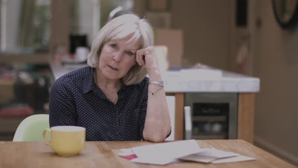 Senior adult woman opening bills at home on kitchen table