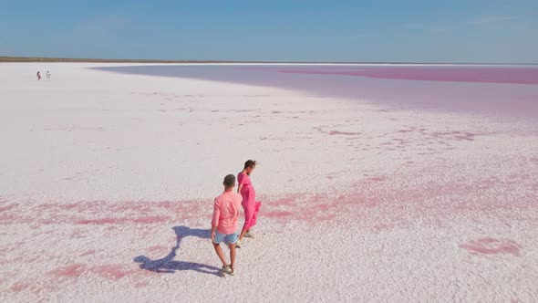 Aerial Drone Footage of Happy Young Couple in Pink Wear Having Fun and Joyfully Running on White alt