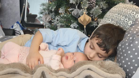 Little brother and newborn sister lie on a bed in Christmas