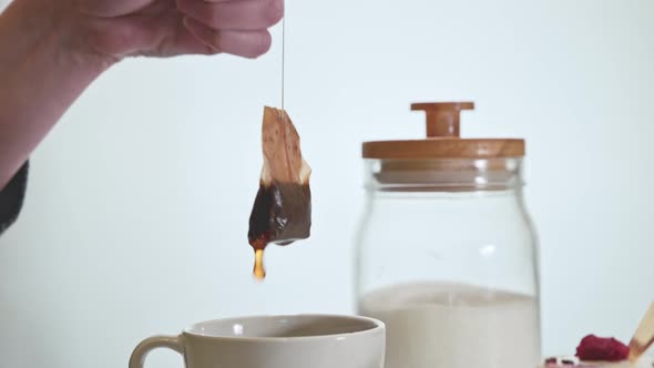 The woman pulls out a tea bag from a mug. Water drips from the tea bag.
