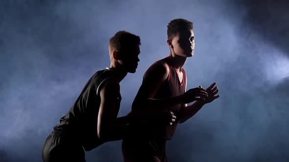 Two Young Athletes Practice Basketball in a Dark Smoky Studio Under the Spotlight alt