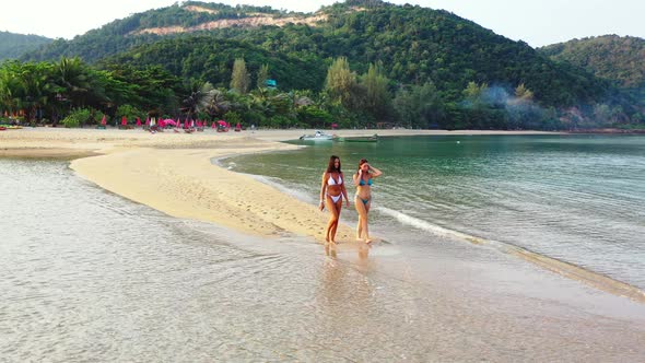 Sexy happy ladies on photoshoot having fun at the beach on sunny blue and white sand background alt