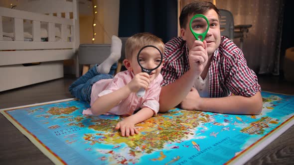 Happy Little Boy with Father Lying on Big Map and Looking Through Magnifying Glass alt