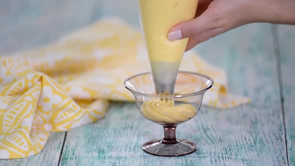 The Chef Is Squeezing The Custard Cream in a glass bowl. alt