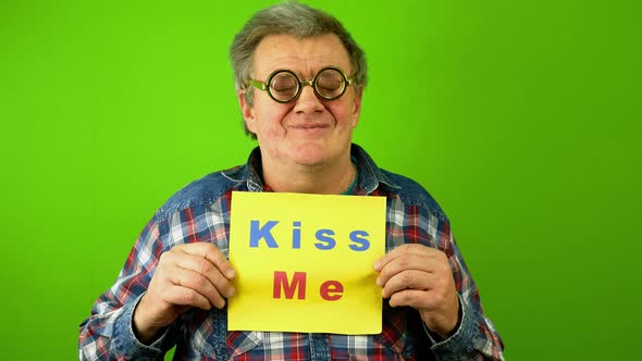 Caucasian Mature Adult Man Smiling and Point Finger at Plaque Lettering Kiss Me alt
